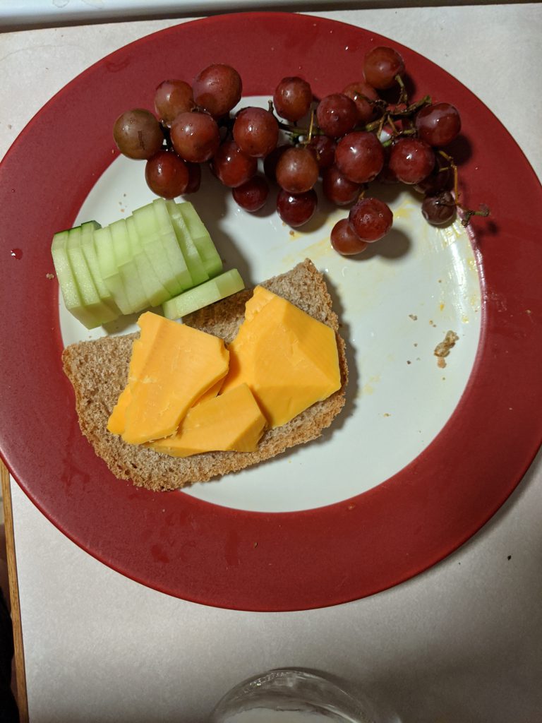 cucumber slices, bread, cheese, and grapes on a plate