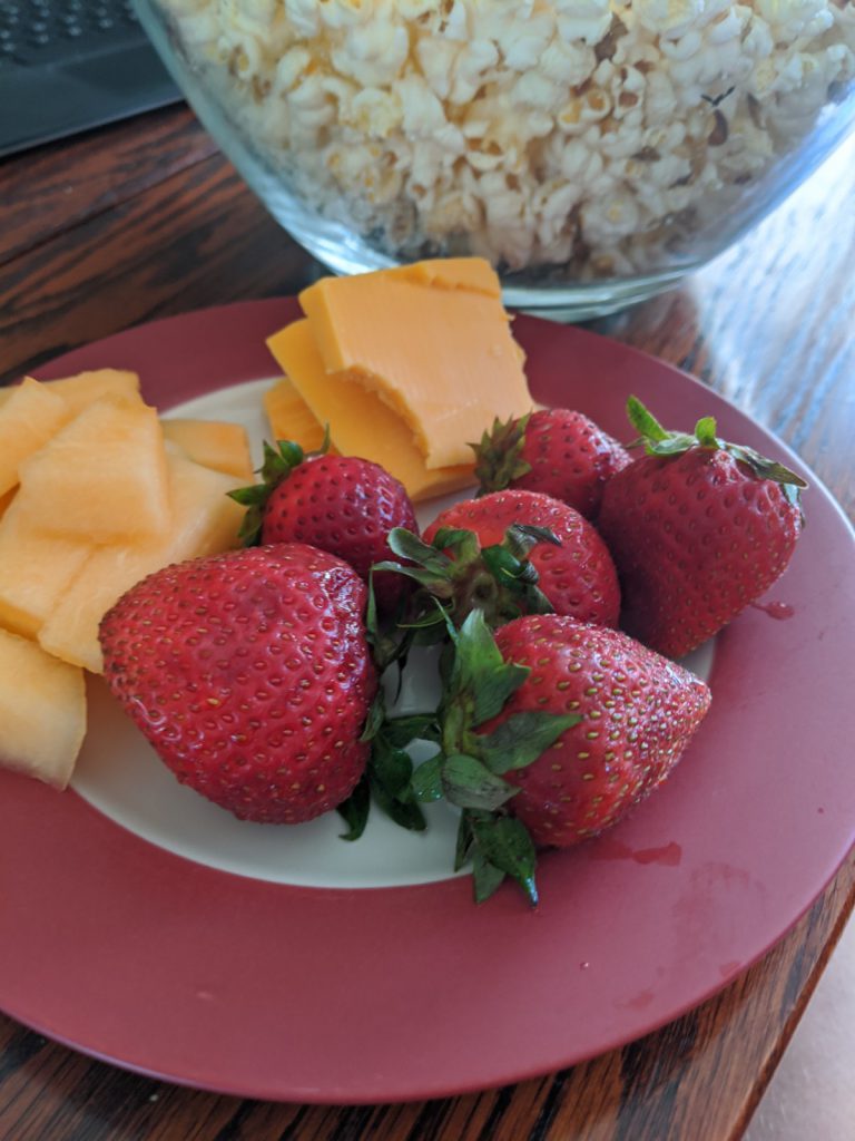 plate with strawberries and cheese and a bowl of popcorn