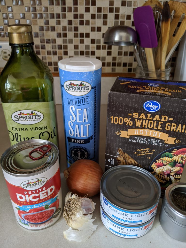 In this picture, there are the ingredients I use: olive oil, canned tomatoes, salt, onion, garlic, tuna, whole wheat pasta, and a container of dried basil