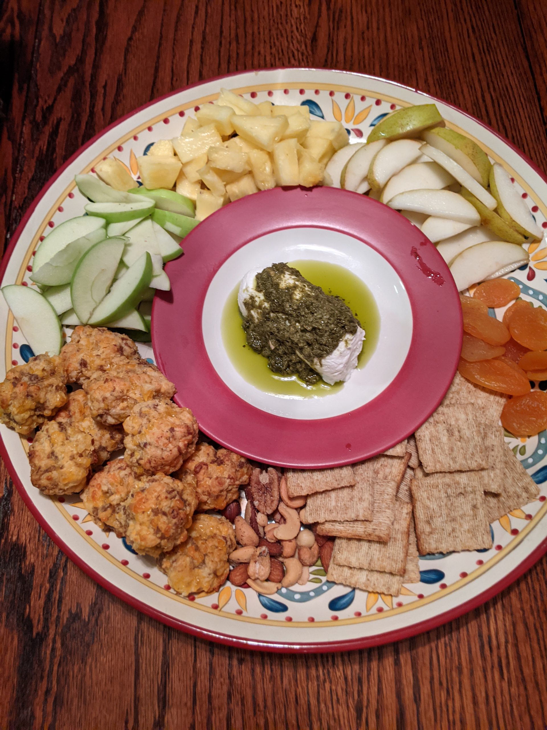 fancy plate with sliced apples, pineapple, pears, dried apricots, crackers, bread puffs, nuts, cheese and sauce