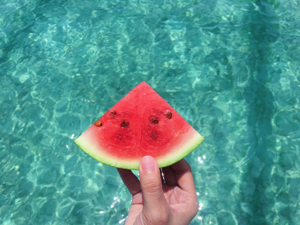 hand holding slice of watermelon over a blue pool