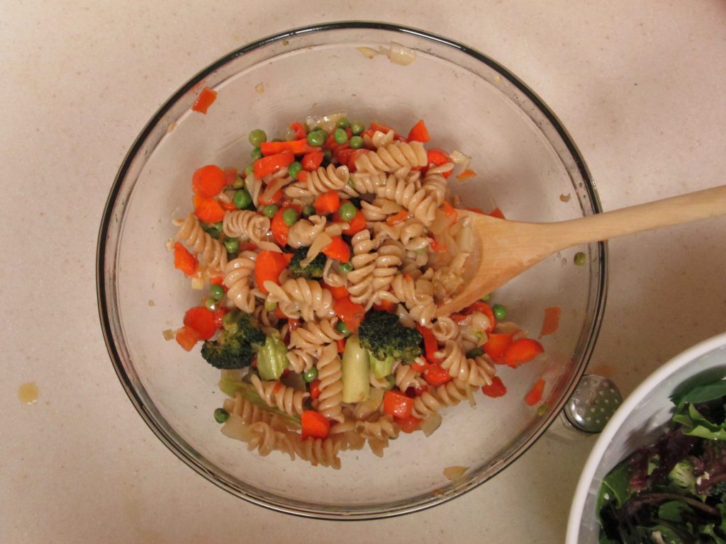 Glass bowl with pasta and carrots and peas and broccoli