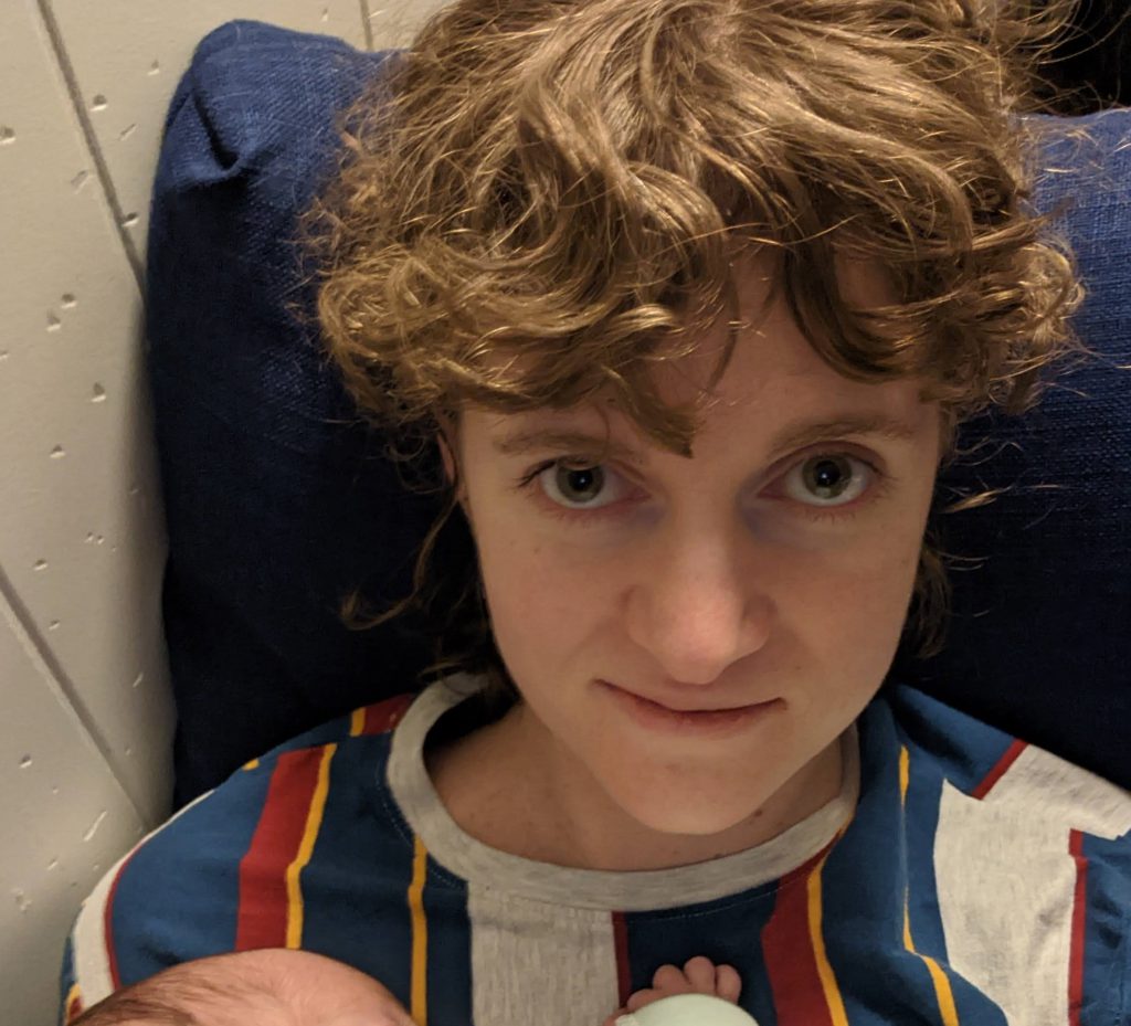 An exhausted woman smiles slightly and holds a newborn